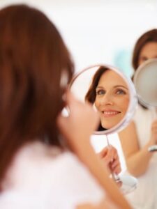 stock image of a woman looking into the mirror for a blog post about custom injectable treatments available with Dr. Brunner in Princeton